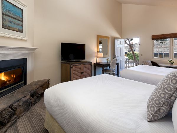 A cozy hotel room with two white beds, a fireplace, a TV, a desk, and a small balcony.