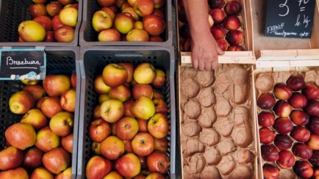 A street market with crates of apples and pears, plus egg cartons and a handwritten price sign on the chalkboard, all arranged in crates.