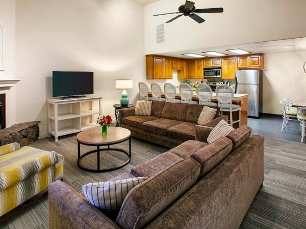 Cozy, open-concept living room with a fireplace, plush sectional, and a modern kitchen with a bar island in the background, bright and inviting.