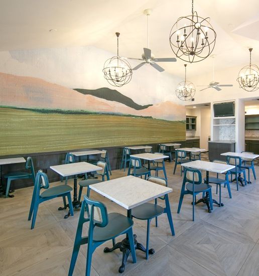 A bright cafe with teal chairs and square tables, a mural of mountains on the wall, modern light fixtures, and a clean indoor dining area.