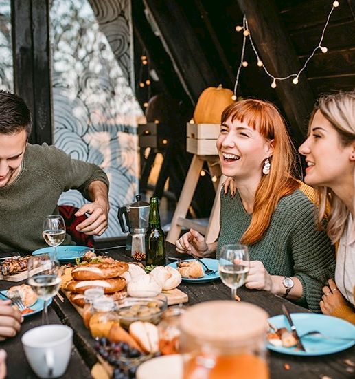 A group of four friends enjoys a casual meal together on a cozy outdoor patio, sharing laughs with coffee, bread, and plates of food.