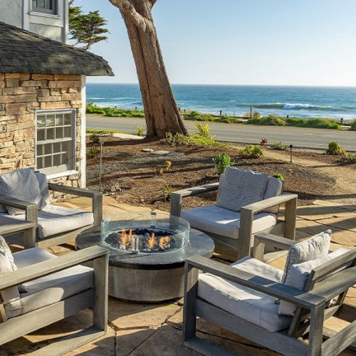 A sunny beachside restaurant with wooden tables, chairs, and umbrellas, overlooking the sea and palm trees.