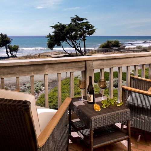 A sunny balcony view with lounge chairs, railing, and a pool or ocean beyond, under a clear blue sky.
