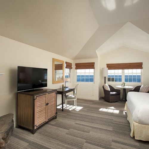 Cozy living room with a fireplace, wood stove, and a bright open area with a dining table and a large windowed wall, bathed in natural light.