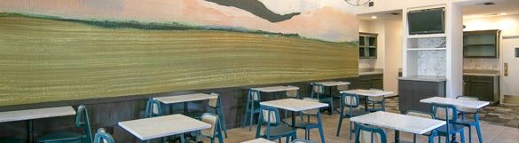 A bright cafe with teal chairs, square tables, a mural of mountains on the wall, modern globe pendant lights, and a clean, airy layout.