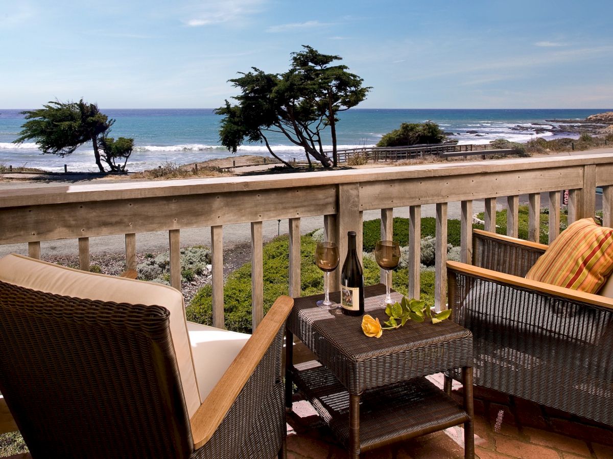 A cozy balcony scene overlooking the beach with two chairs, a small table, wine, and scenic ocean views, perfect for sunset refreshments.