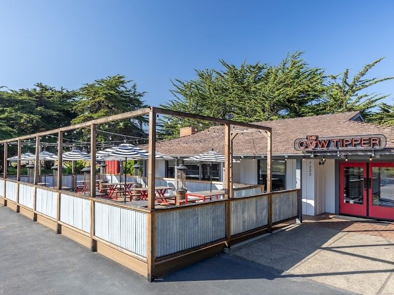 A small restaurant with a wooden-framed, partially enclosed deck, red doors, and outdoor seating under a clear blue sky.