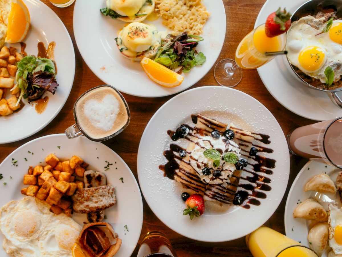 A delicious brunch spread with eggs, toast, potatoes, fruit, pancakes, desserts, and drinks all on a wooden table.